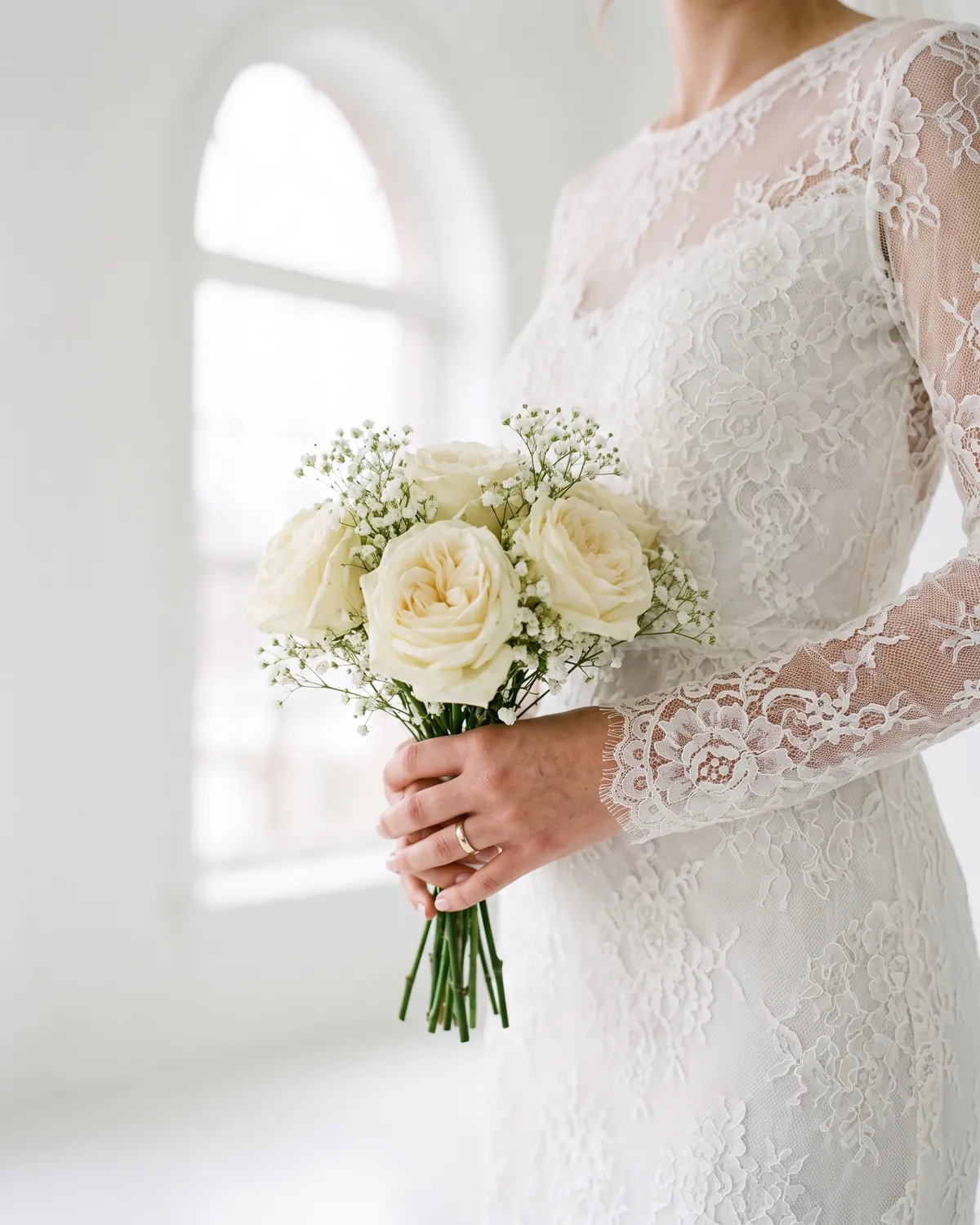 The bride's bouquet of white roses and gypsophila against her lace sleeves