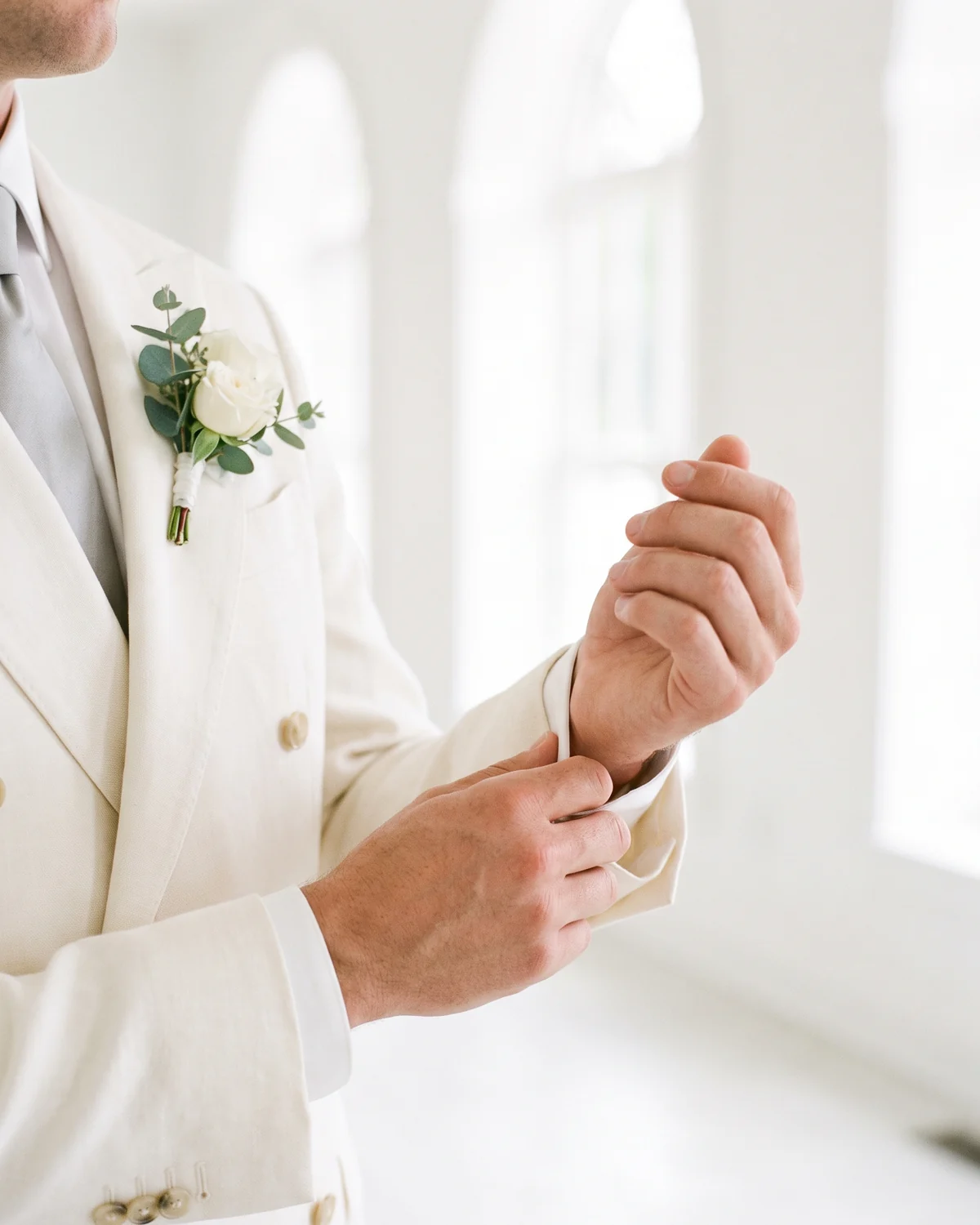 The groom fastening his cuff, a white rose in his buttonhole