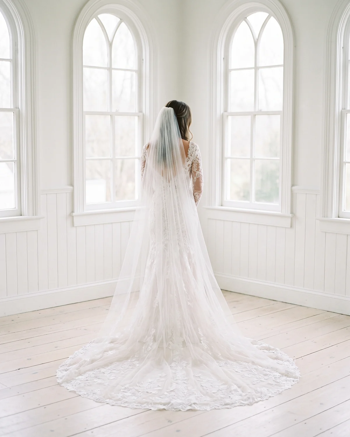 The bride at a tall arched window, her veil across the floorboards